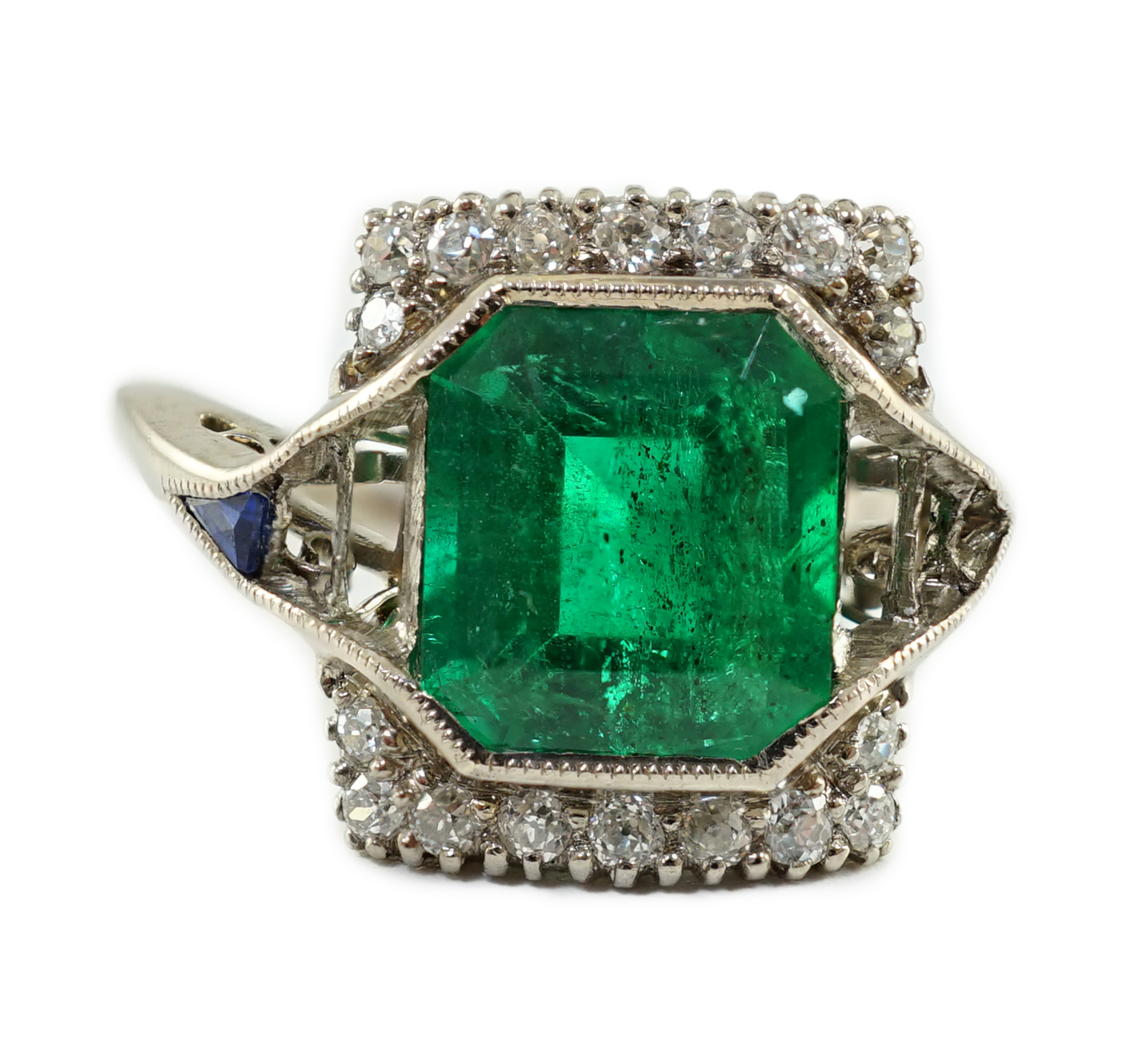 An Art Deco 18k white gold, emerald and diamond set square cluster dress ring, with shaped cut sapphire set shoulders, (a.f.)